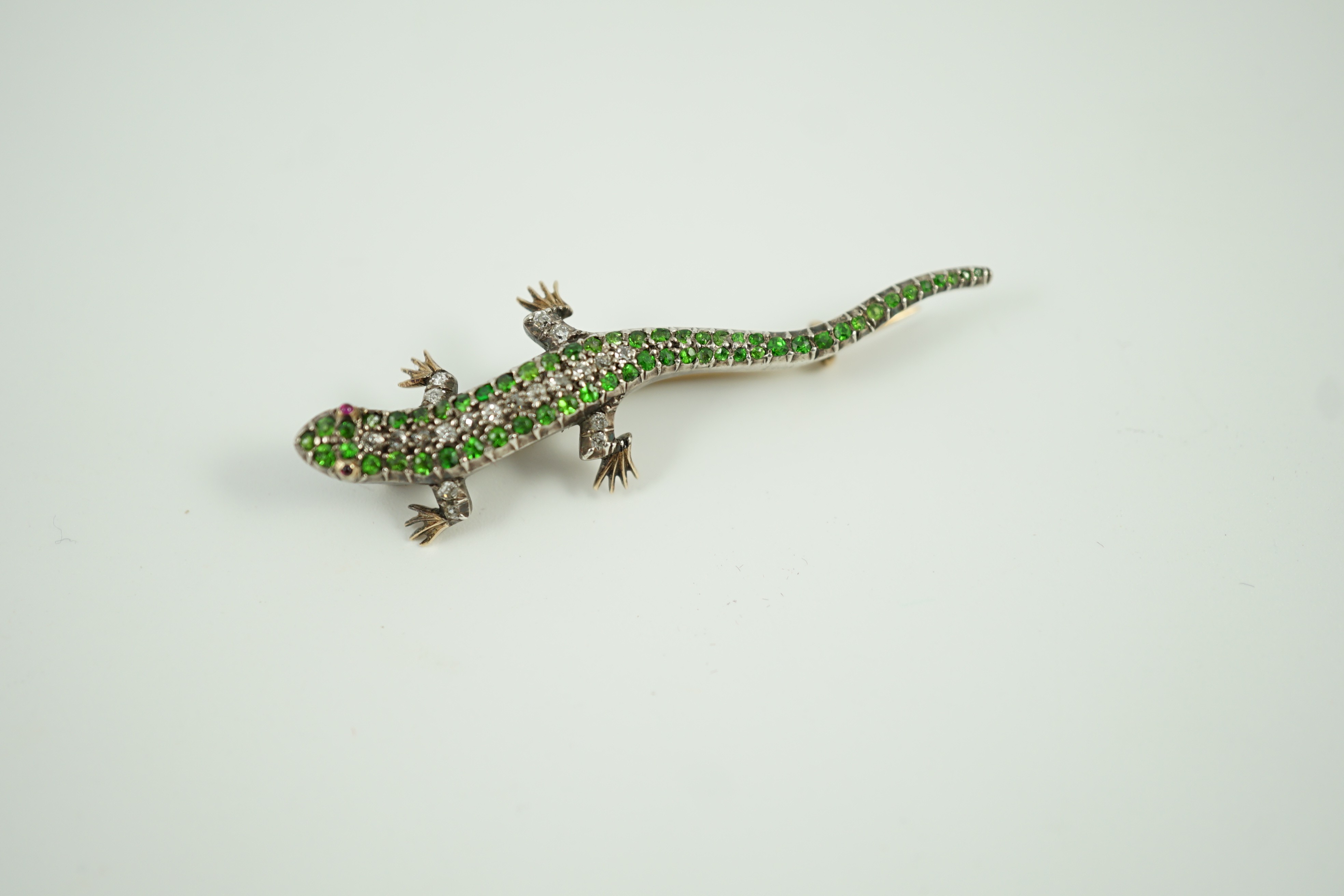 An Edwardian yellow metal, diamond and green garnet set lizard brooch, with red cabochon eyes, 50mm, gross weight 6.2 grams.